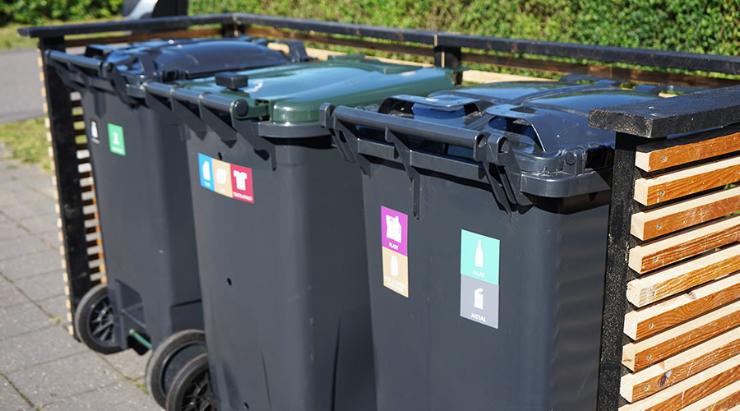 Tre affaldsbeholdere med piktogrammer står i skjul